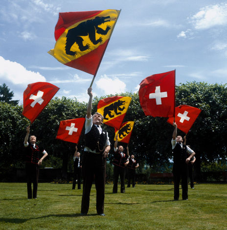 Участники швейцарского фольклорного фестиваля по традиции размахивают флагами и играют на традиционном швейцарском духовом музыкальном инструменте Альпийский рог.