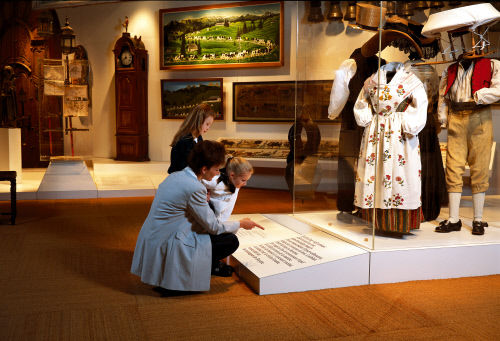 Мама с ребенком напротив музейной витрины, где показан традиционный костюм региона Грюйер (Gruerien) в музее, в кантоне Фрибур (Fribourg)